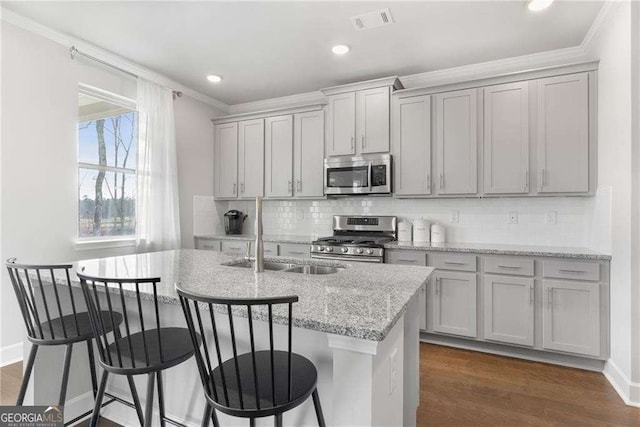 kitchen featuring ornamental molding, a kitchen island with sink, visible vents, appliances with stainless steel finishes, and a sink