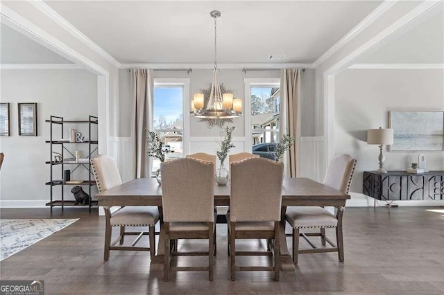 dining room with dark wood-style flooring, a chandelier, crown molding, wainscoting, and a decorative wall