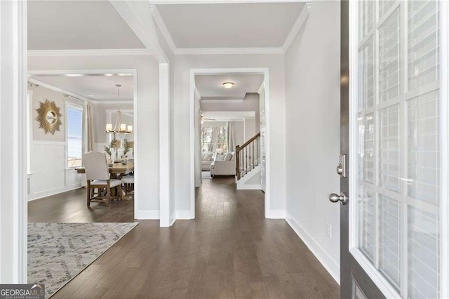 foyer entrance with a notable chandelier, baseboards, ornamental molding, stairway, and dark wood-type flooring
