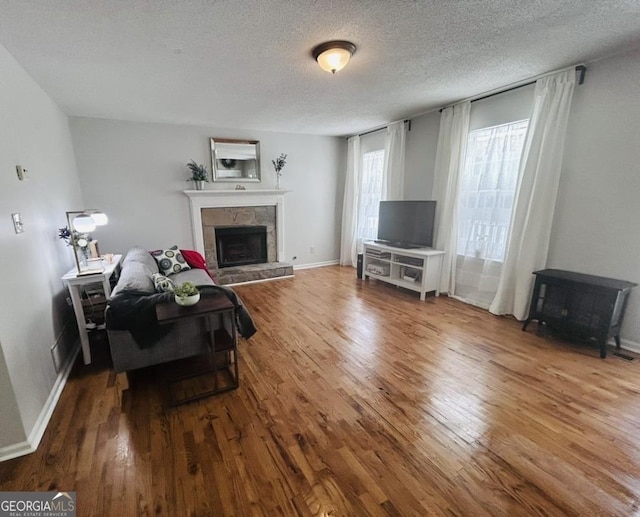 living room with a textured ceiling, a stone fireplace, a wood stove, wood finished floors, and baseboards