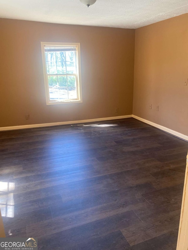 spare room with baseboards and dark wood-style floors