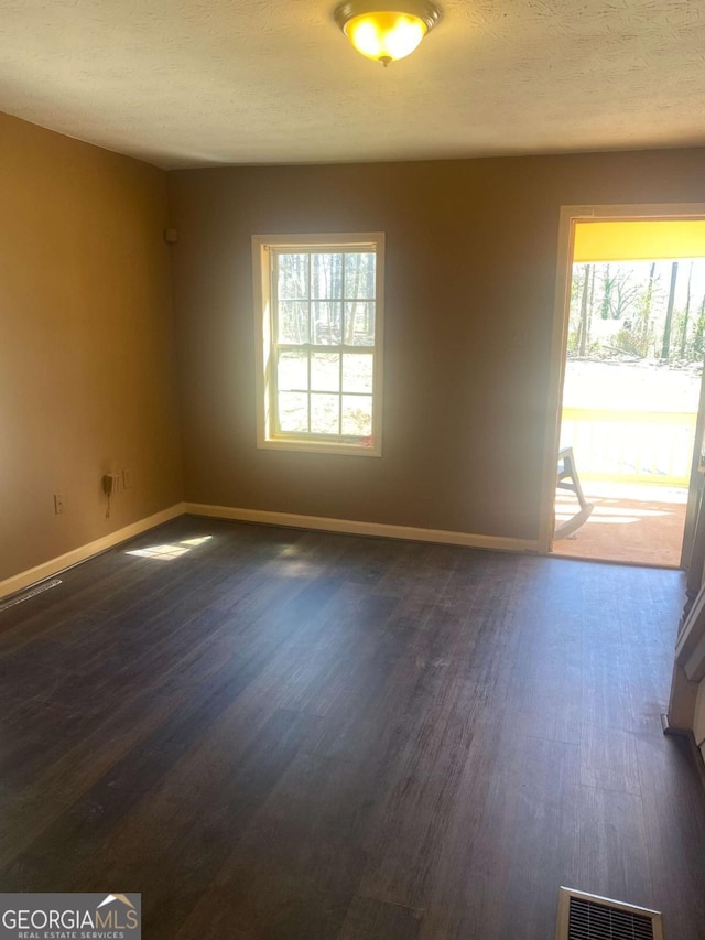 spare room with a healthy amount of sunlight, baseboards, dark wood finished floors, and visible vents