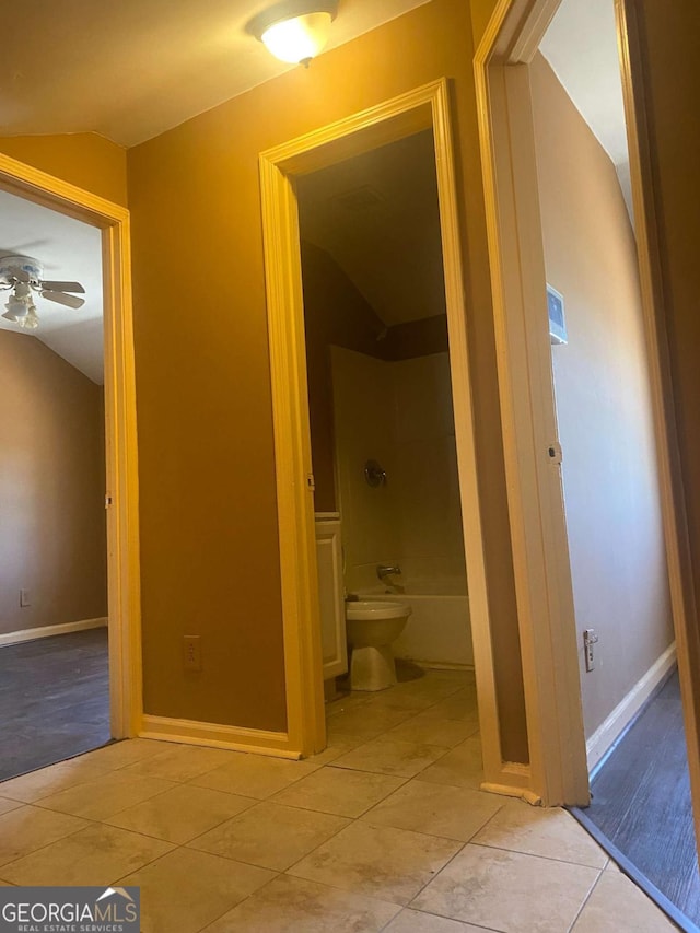 hall with tile patterned flooring, baseboards, and vaulted ceiling