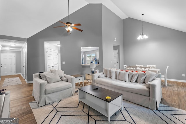 living room with baseboards, high vaulted ceiling, wood finished floors, and ceiling fan with notable chandelier