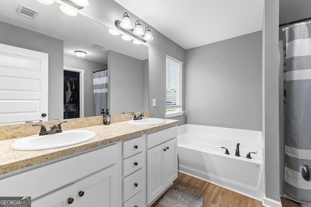 bathroom with a sink, double vanity, wood finished floors, and visible vents