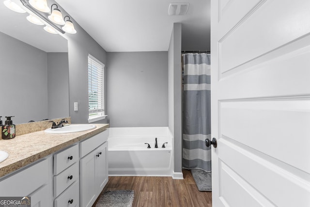 full bath featuring a sink, double vanity, wood finished floors, visible vents, and a bath