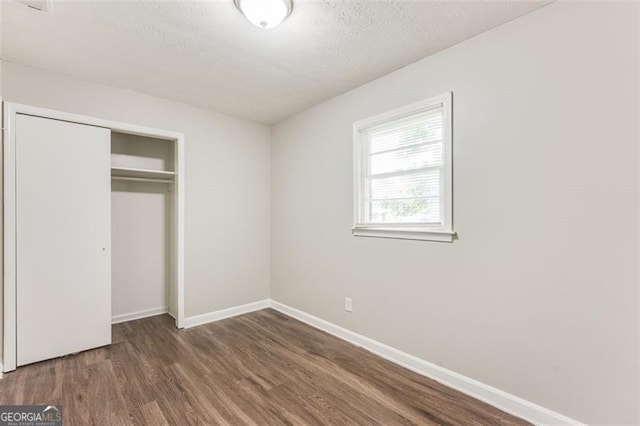 unfurnished bedroom featuring a textured ceiling, a closet, baseboards, and wood finished floors