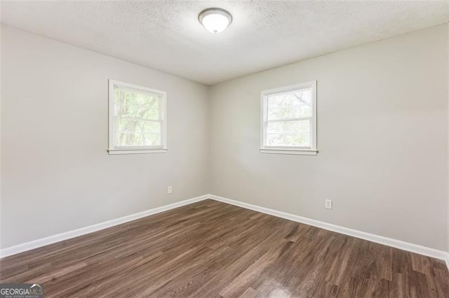 empty room with dark wood-style flooring, baseboards, and a healthy amount of sunlight