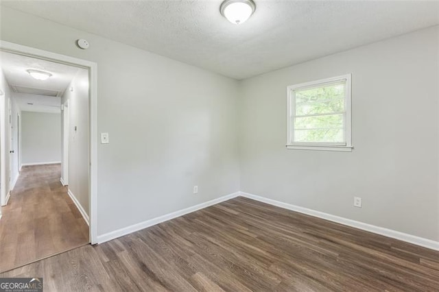 unfurnished room with wood finished floors, attic access, and baseboards