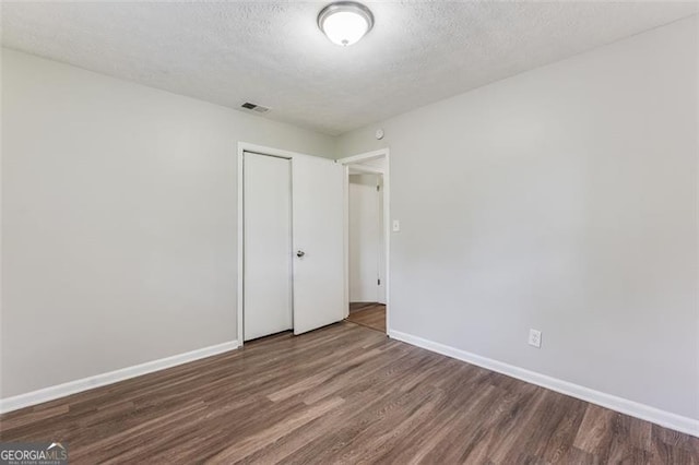 unfurnished bedroom with dark wood-type flooring, a closet, baseboards, and visible vents