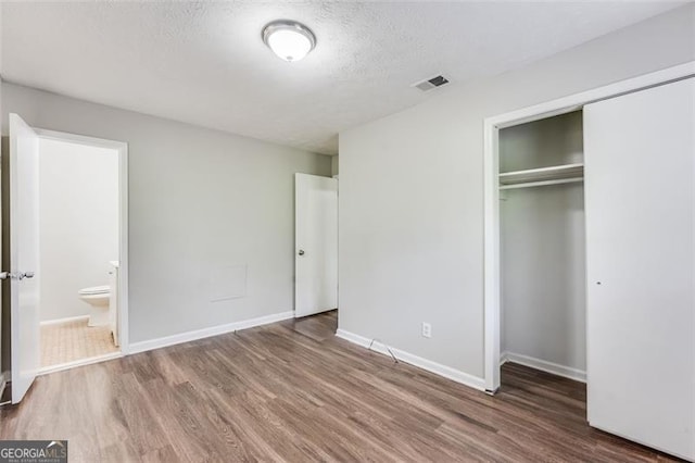 unfurnished bedroom featuring baseboards, wood finished floors, a closet, and visible vents