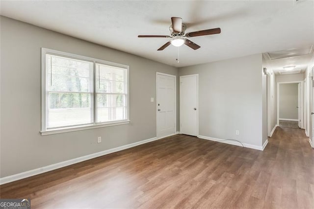 spare room featuring attic access, baseboards, a ceiling fan, and wood finished floors