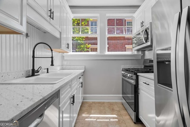 kitchen featuring baseboards, a sink, white cabinetry, stainless steel appliances, and light tile patterned flooring