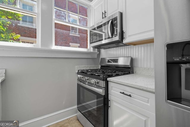 kitchen with stainless steel appliances, light tile patterned floors, white cabinets, and light stone counters