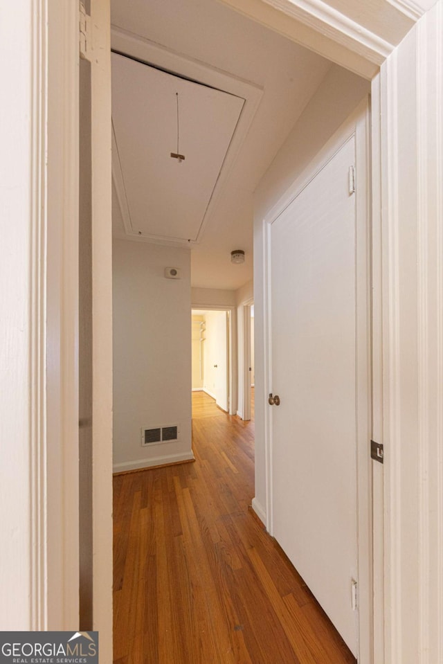 hallway with visible vents, attic access, and wood finished floors