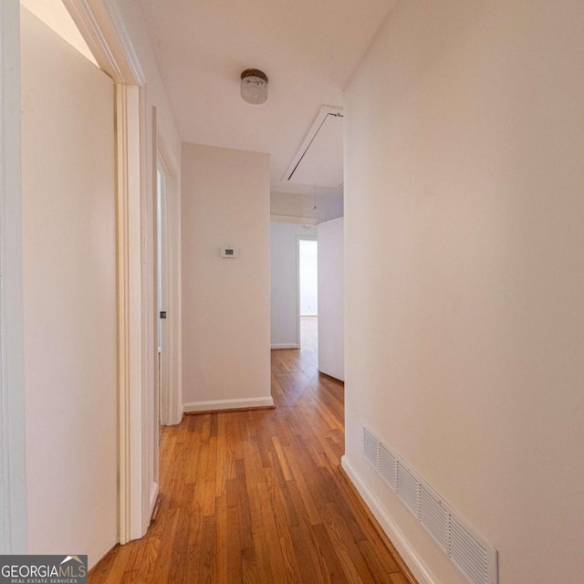 hall featuring light wood-style flooring, attic access, baseboards, and visible vents