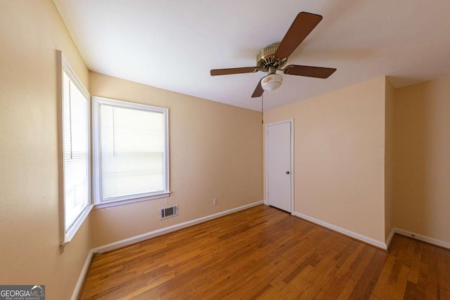 empty room with visible vents, a wealth of natural light, wood finished floors, and baseboards