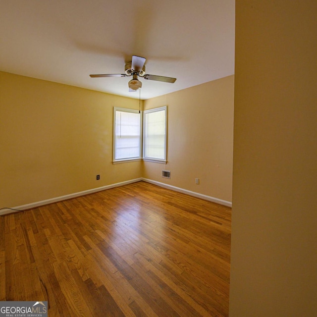 empty room featuring wood finished floors, baseboards, a ceiling fan, and visible vents