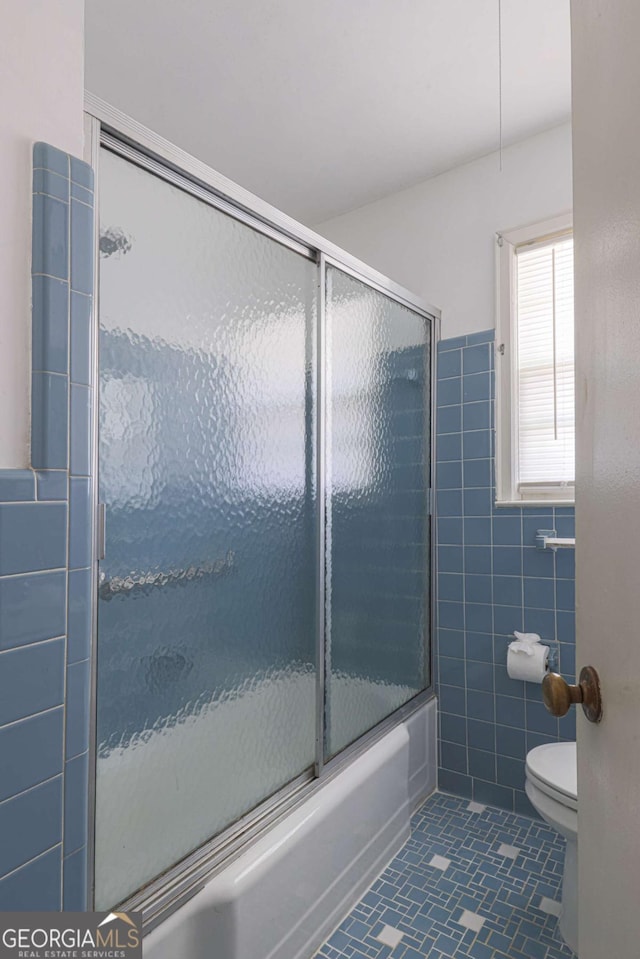 full bath featuring combined bath / shower with glass door, tile patterned flooring, tile walls, and toilet