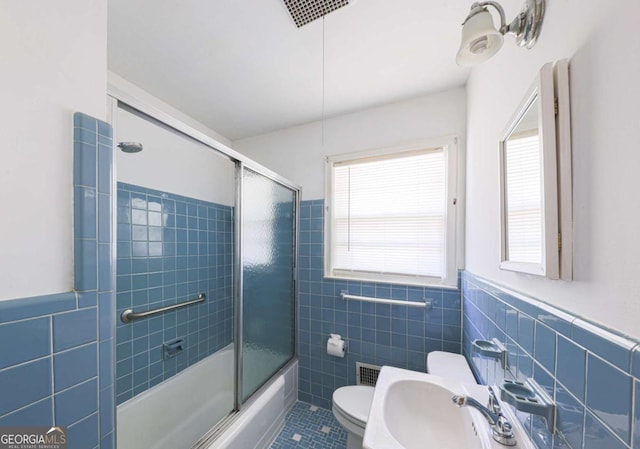 bathroom featuring tile patterned flooring, toilet, a sink, combined bath / shower with glass door, and tile walls