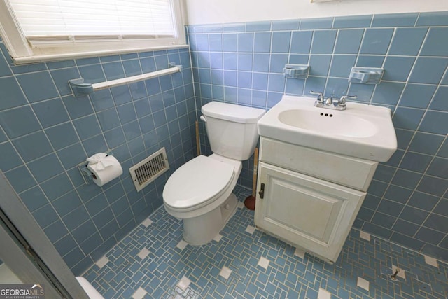 half bath featuring vanity, visible vents, tile walls, and toilet