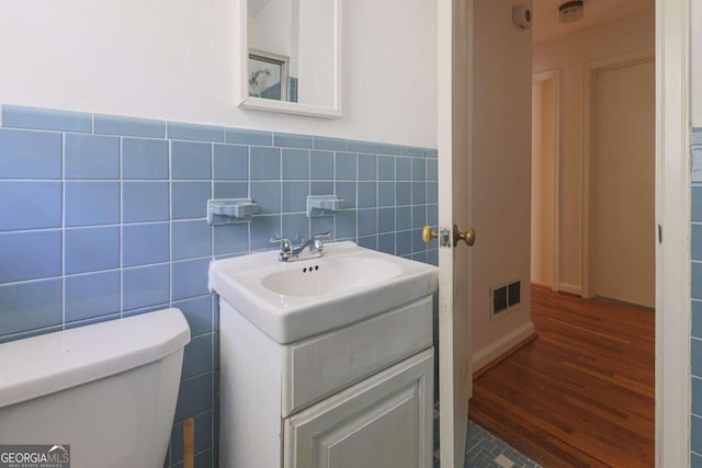 half bathroom with vanity, visible vents, toilet, wood finished floors, and tile walls
