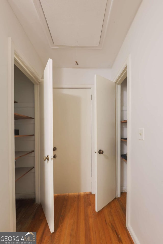 hallway featuring attic access and wood finished floors