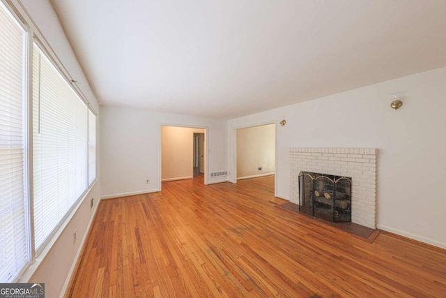 unfurnished living room featuring baseboards, a brick fireplace, light wood-type flooring, and visible vents