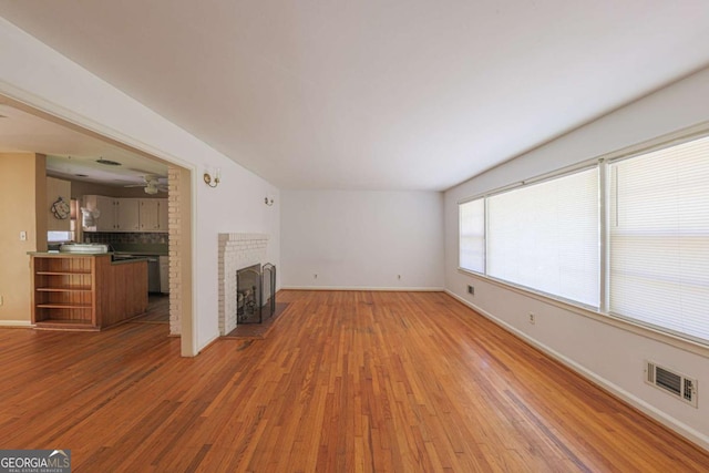 unfurnished living room with a brick fireplace, visible vents, a ceiling fan, and light wood-style flooring