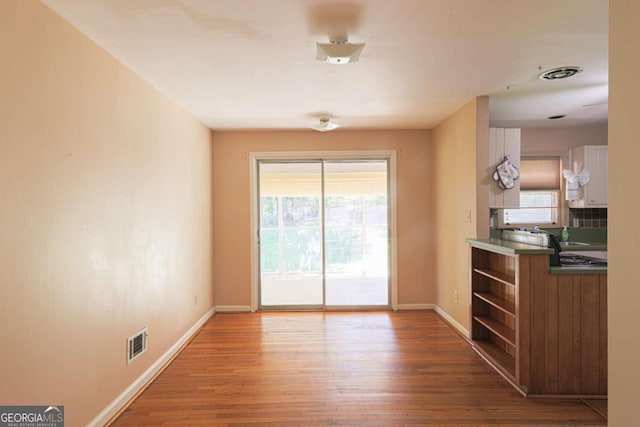 unfurnished dining area with wood finished floors, baseboards, and visible vents