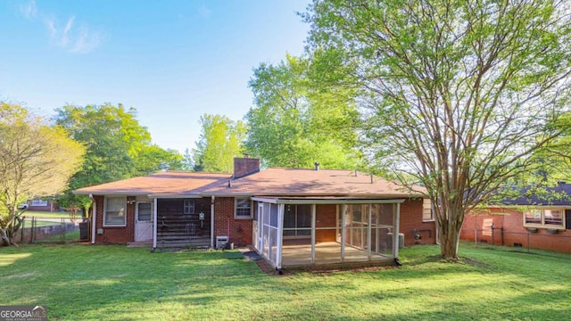back of house featuring a chimney, brick siding, a fenced backyard, a sunroom, and a lawn