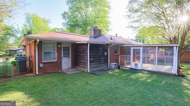 back of property with brick siding, a chimney, a sunroom, and a lawn