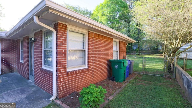 view of side of home with brick siding, fence, and a lawn