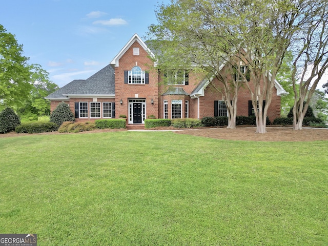 view of front of home with a shingled roof, brick siding, and a front lawn