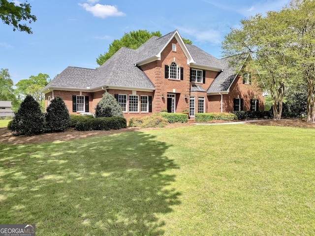 view of front of house with a shingled roof, a front yard, and brick siding