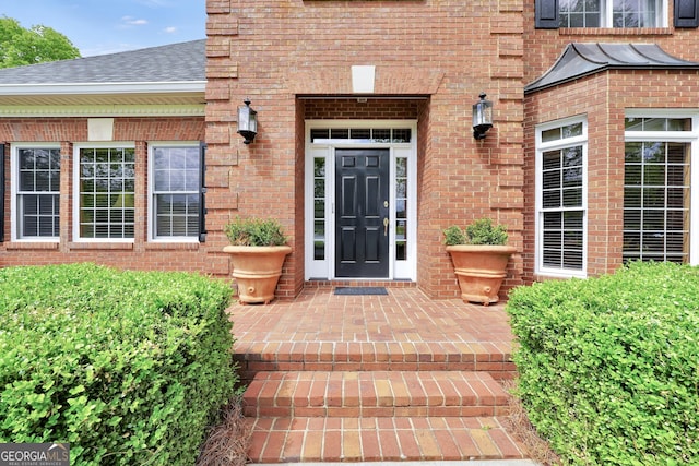 doorway to property featuring brick siding and a shingled roof