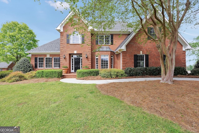 view of front of home with brick siding, a front lawn, and roof with shingles