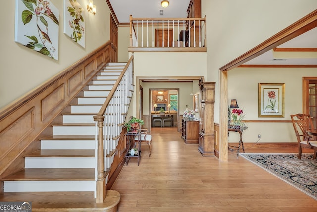 entrance foyer featuring stairs, light wood finished floors, a towering ceiling, and crown molding