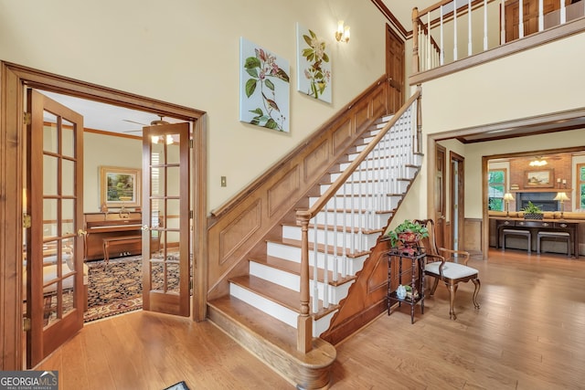 staircase with crown molding, french doors, a towering ceiling, and wood finished floors