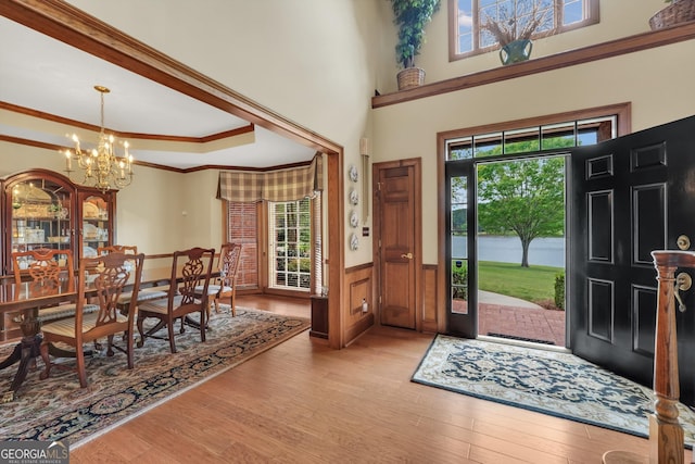 entryway with a chandelier, ornamental molding, plenty of natural light, and a wainscoted wall
