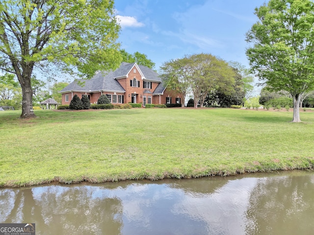 view of front facade with a front yard, a water view, and brick siding