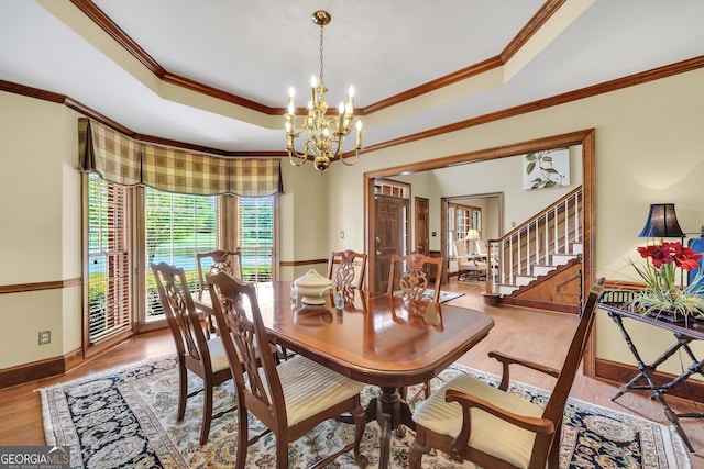 dining space with crown molding, a tray ceiling, an inviting chandelier, and wood finished floors