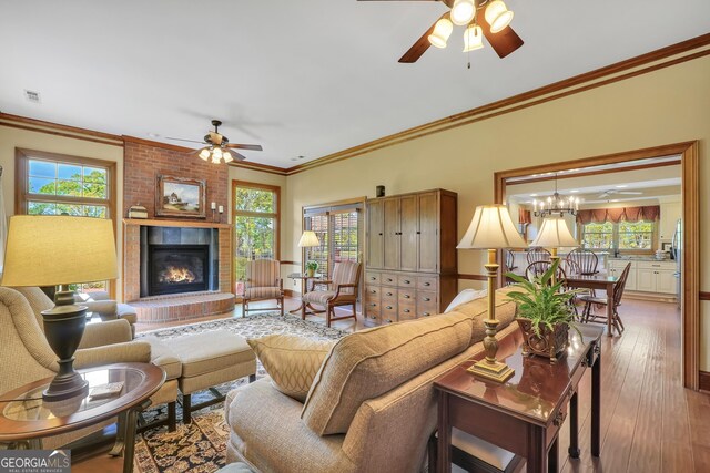 living room with crown molding, ceiling fan with notable chandelier, a fireplace, and a wealth of natural light