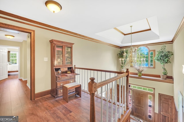corridor featuring a raised ceiling, an upstairs landing, a chandelier, and wood finished floors