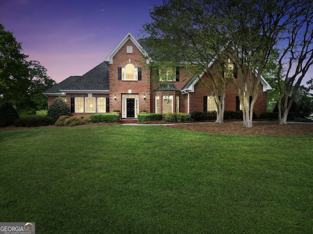 view of front of property with roof with shingles, a lawn, and brick siding