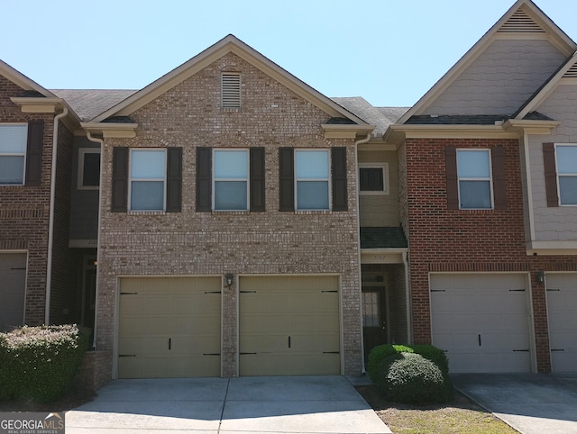 townhome / multi-family property featuring brick siding, an attached garage, driveway, and roof with shingles