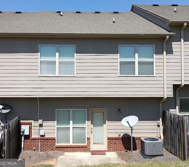 rear view of property with fence, cooling unit, and roof with shingles