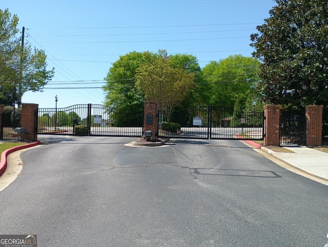 view of road featuring curbs, a gated entry, a gate, and sidewalks