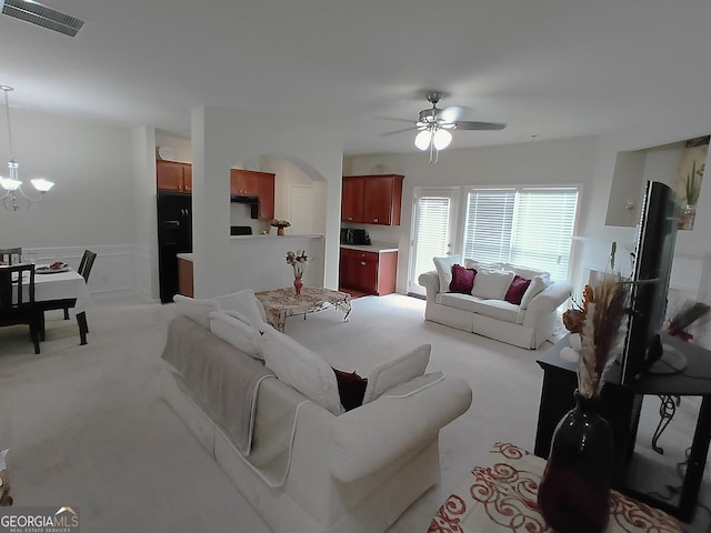 living area featuring ceiling fan with notable chandelier, arched walkways, light colored carpet, visible vents, and a wainscoted wall