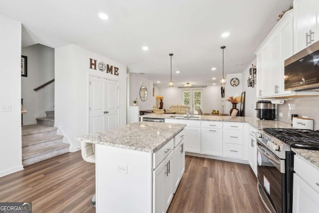 kitchen with stainless steel appliances, a peninsula, wood finished floors, and open floor plan